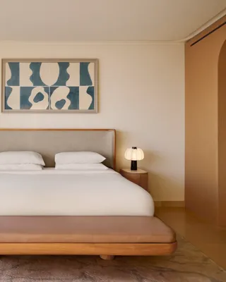 Chambre contemporaine avec grand lit, banc rembourré et œuvre abstraite au-dessus, complétée par des finitions en bois chaleureux et un éclairage doux.
