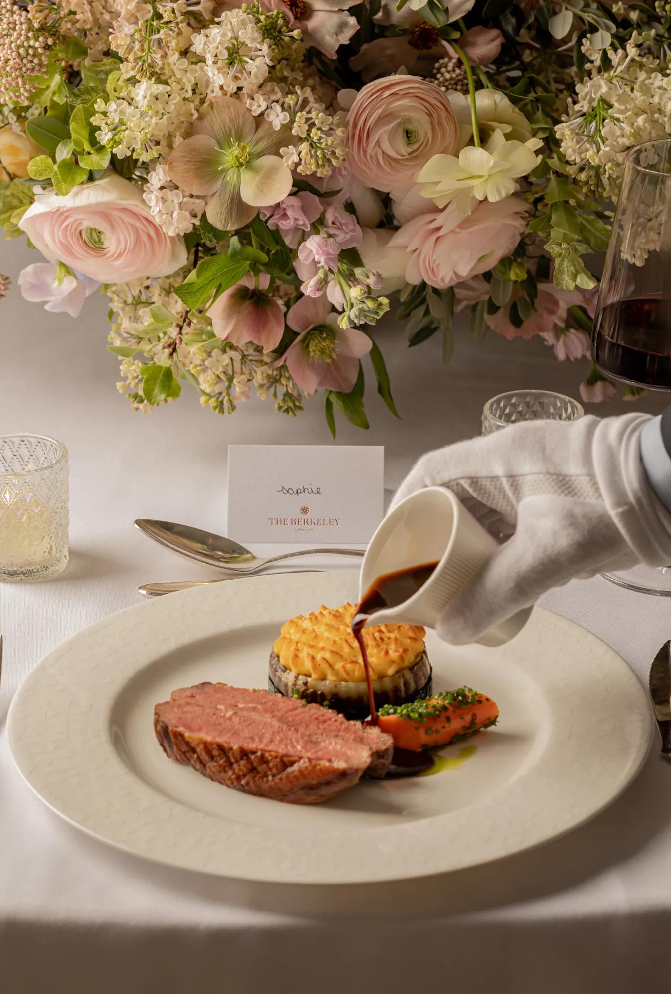 A gloved hand pouring sauce over a dish