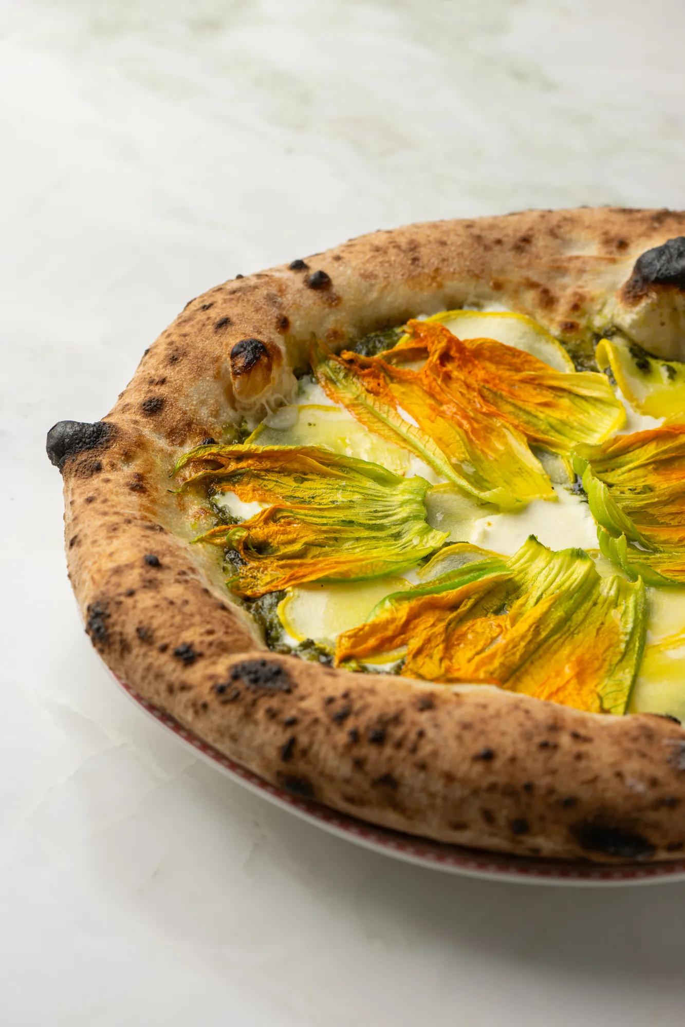 Wood-fired Dante pizza topped with zucchini blossoms and melted cheese on marble surface.
