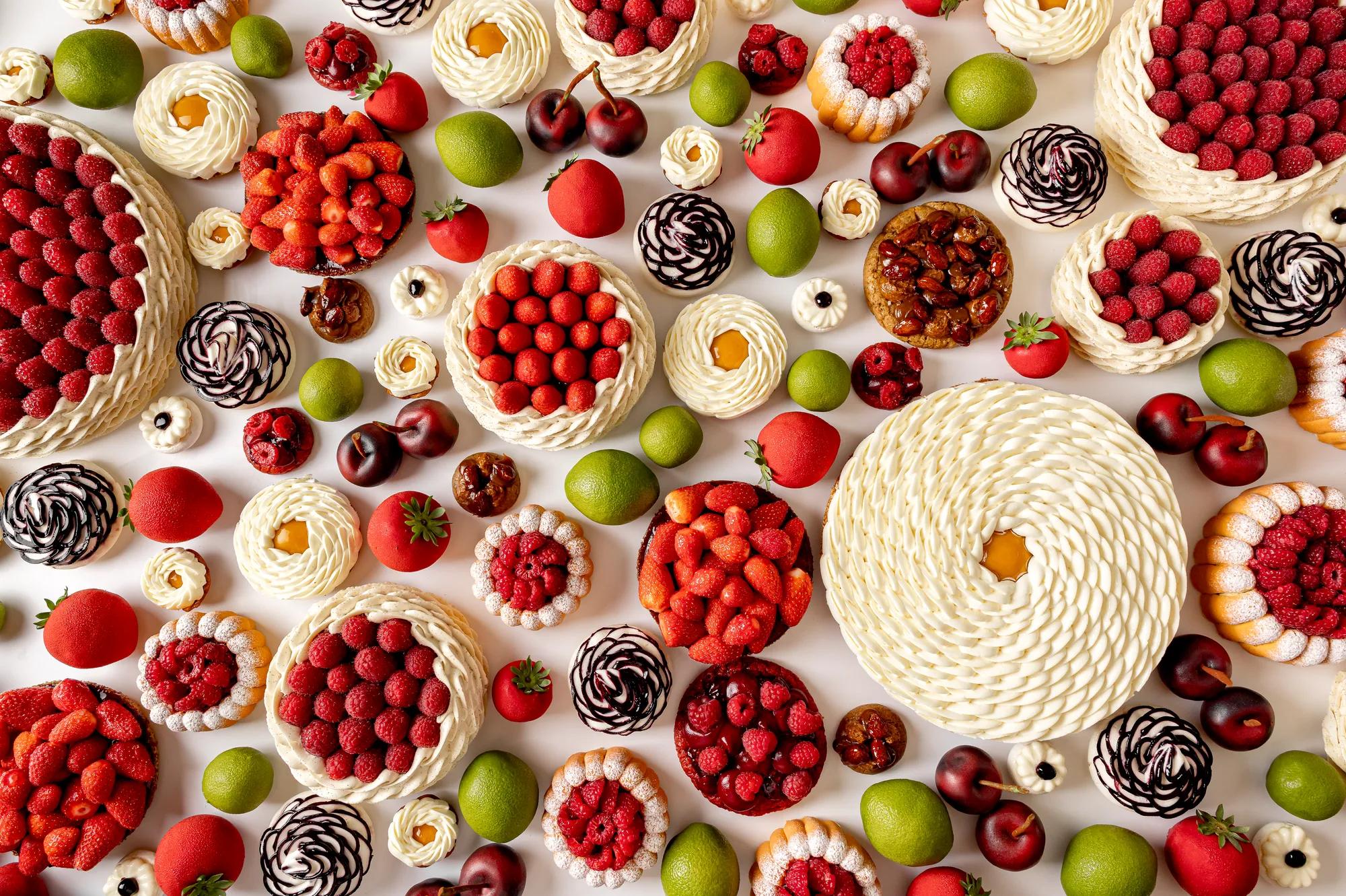 Overhead view of intricate fruit-themed pastries in red, green, and white tones on a white surface.