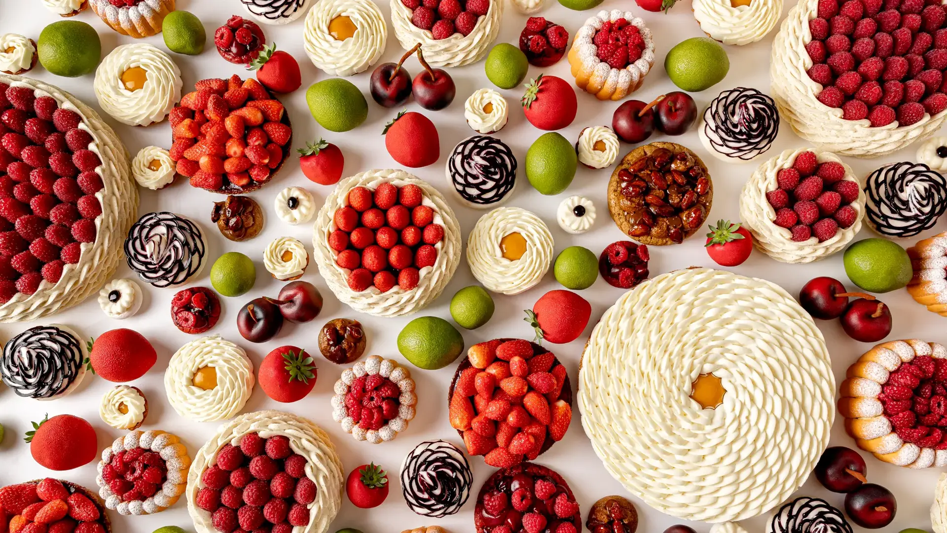 Overhead view of intricate fruit-themed pastries in red, green, and white tones on a white surface.