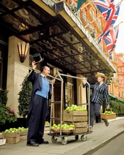 Claridge's hotel entrance with Union flags, staff, and crates of green apples outside.