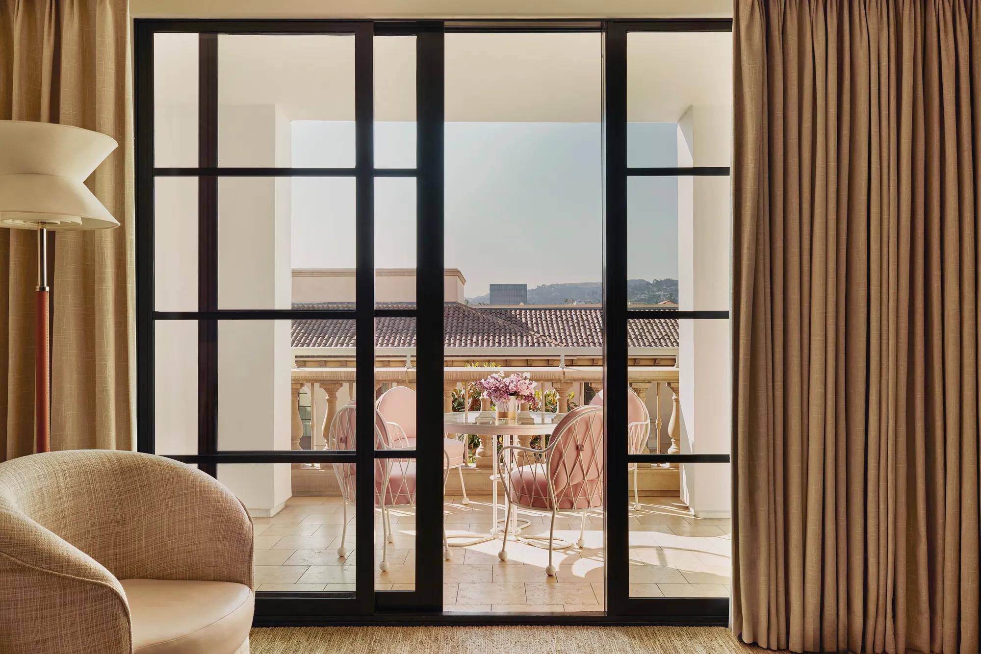 Terrace seen through sliding doors: round table with flowers and four cushioned chairs, with tiled roofs and hills beyond.