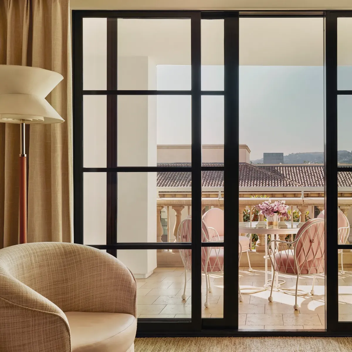 Terrace seen through sliding doors: round table with flowers and four cushioned chairs, with tiled roofs and hills beyond.