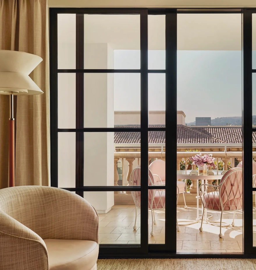 Terrace seen through sliding doors: round table with flowers and four cushioned chairs, with tiled roofs and hills beyond.