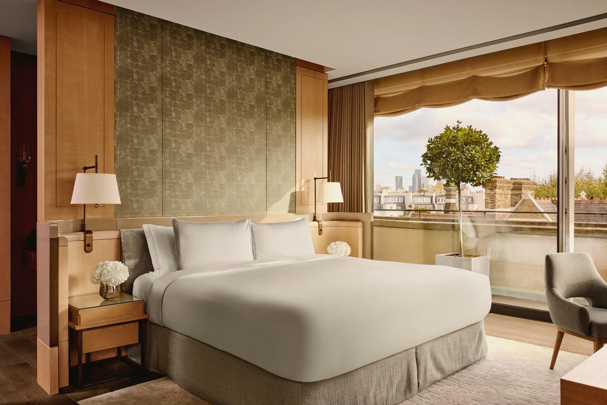 Penthouse bedroom with king bed, soft lighting, and large windows overlooking rooftops and skyline
