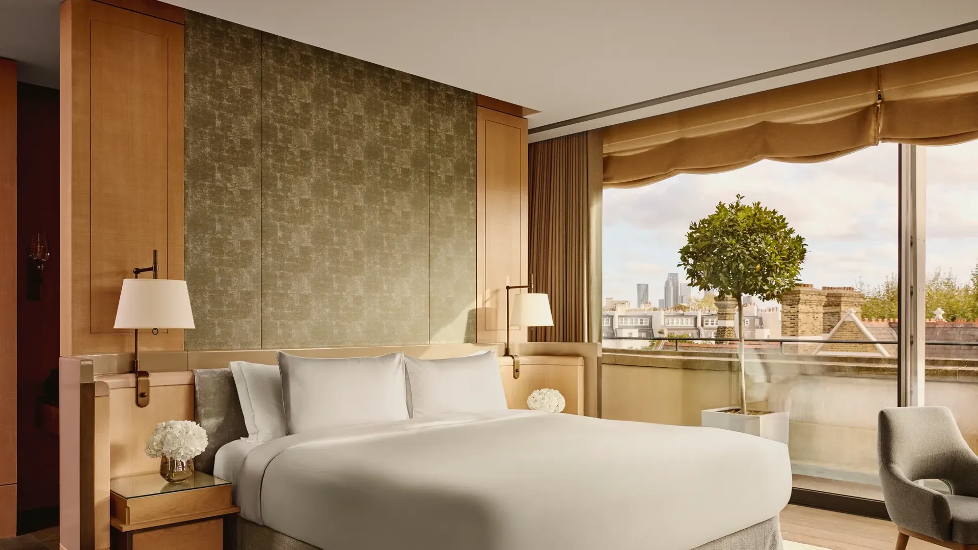 Penthouse bedroom with king bed, soft lighting, and large windows overlooking rooftops and skyline