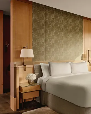 Penthouse bedroom with king bed, soft lighting, and large windows overlooking rooftops and skyline