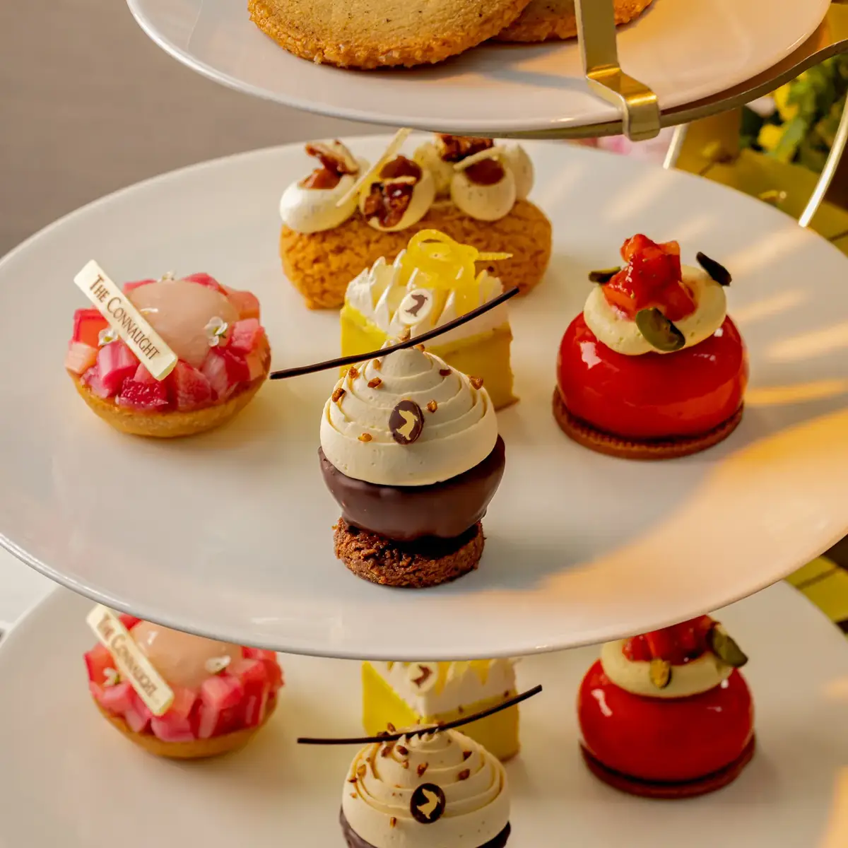 Tiered stand of colorful pastries and cakes, including glossy domed desserts and piped cream sweets on white plates.
