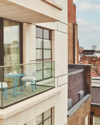 Private balcony with bistro table and chairs, glass balustrade, open doors to bedroom, and city rooftops beyond.