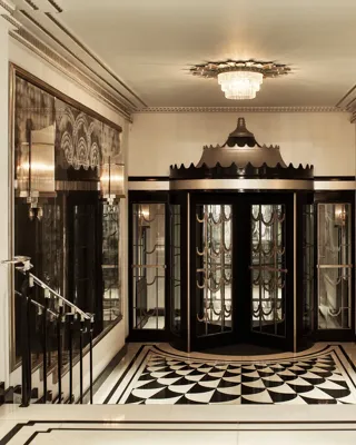 Art Deco revolving door entrance at Claridge’s, featuring black and gold detailing, mirrored walls, geometric black-and-white floor tiles, and a crystal chandelier overhead.
