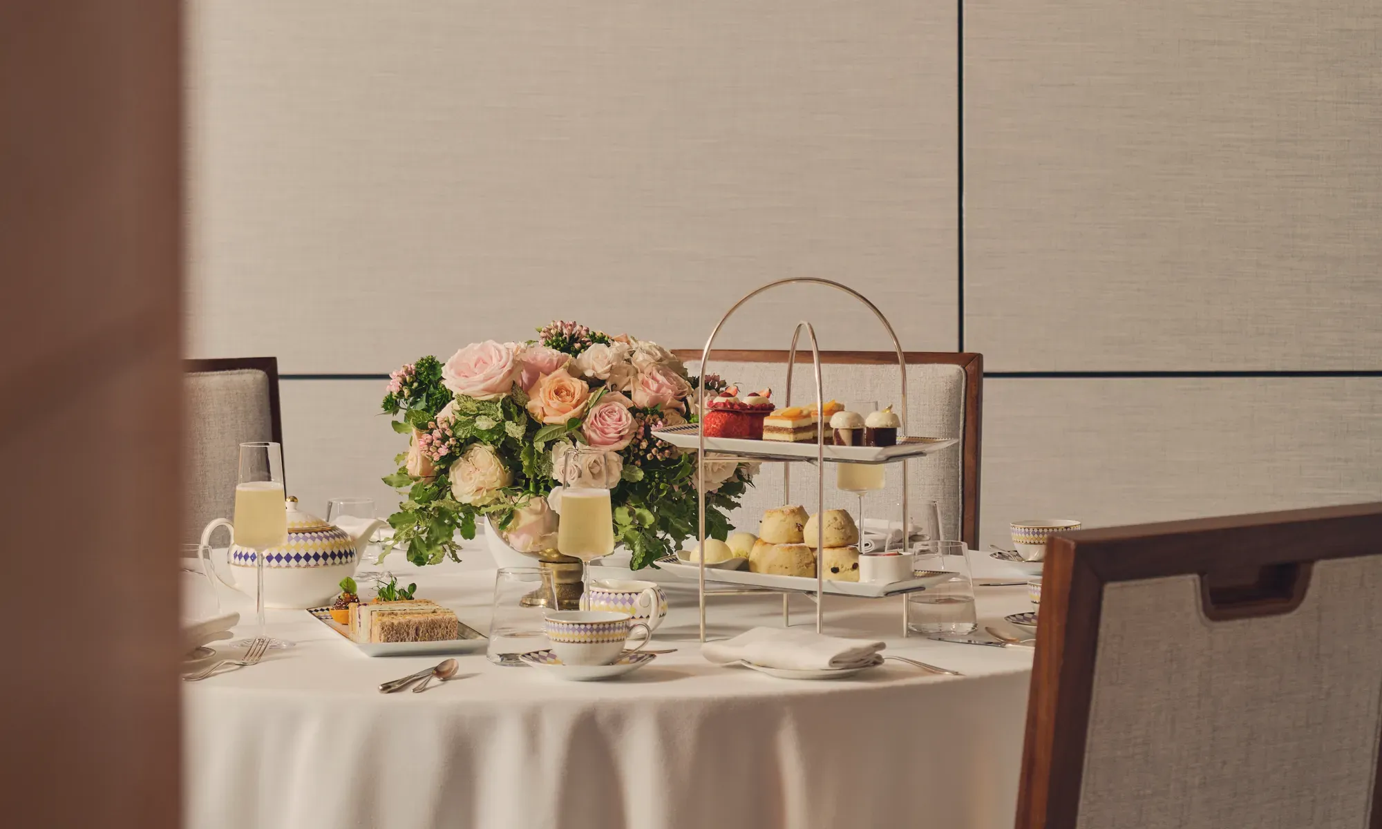 Afternoon tea table with tiered stand of pastries, teacups, champagne, and a floral centerpiece.