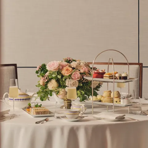 Afternoon tea table with tiered stand of pastries, teacups, champagne, and a floral centerpiece.