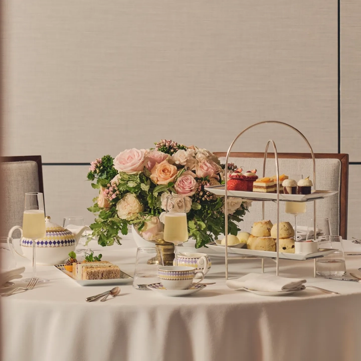 Afternoon tea table with tiered stand of pastries, teacups, champagne, and a floral centerpiece.