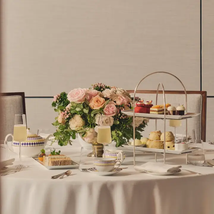 Afternoon tea table with tiered stand of pastries, teacups, champagne, and a floral centerpiece.