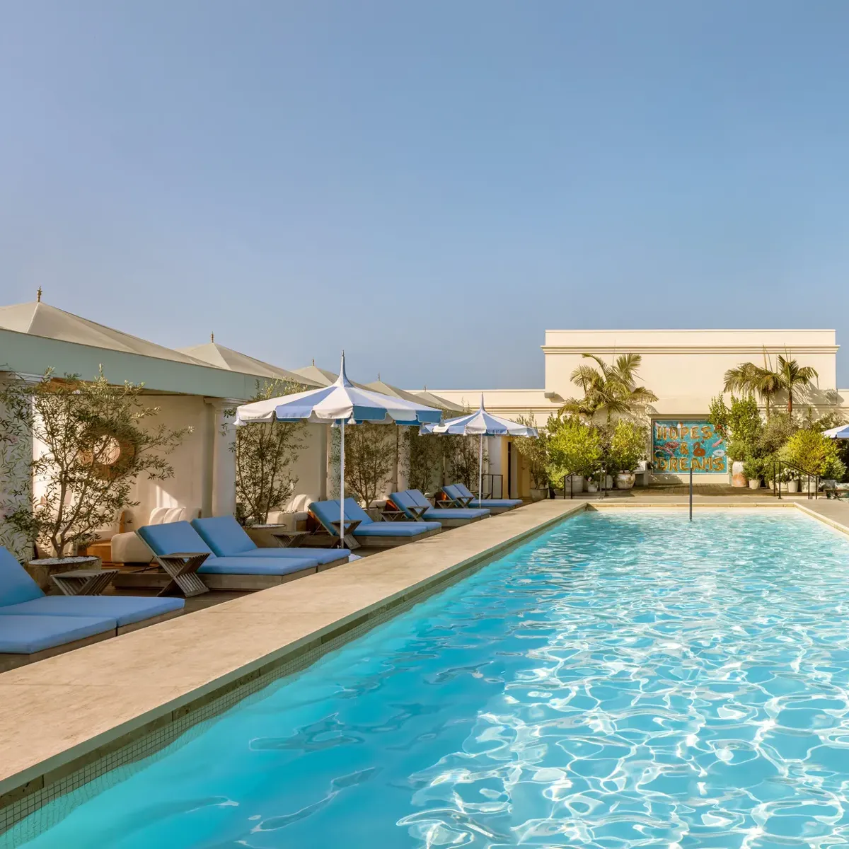 Lap-style rooftop pool at The Maybourne Beverly Hills lined with cabanas and blue-and-white umbrellas.