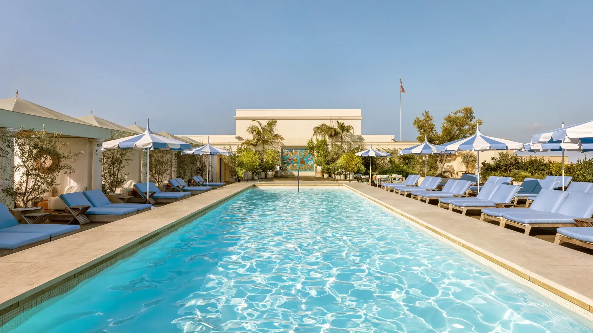 Lap-style rooftop pool at The Maybourne Beverly Hills lined with cabanas and blue-and-white umbrellas.