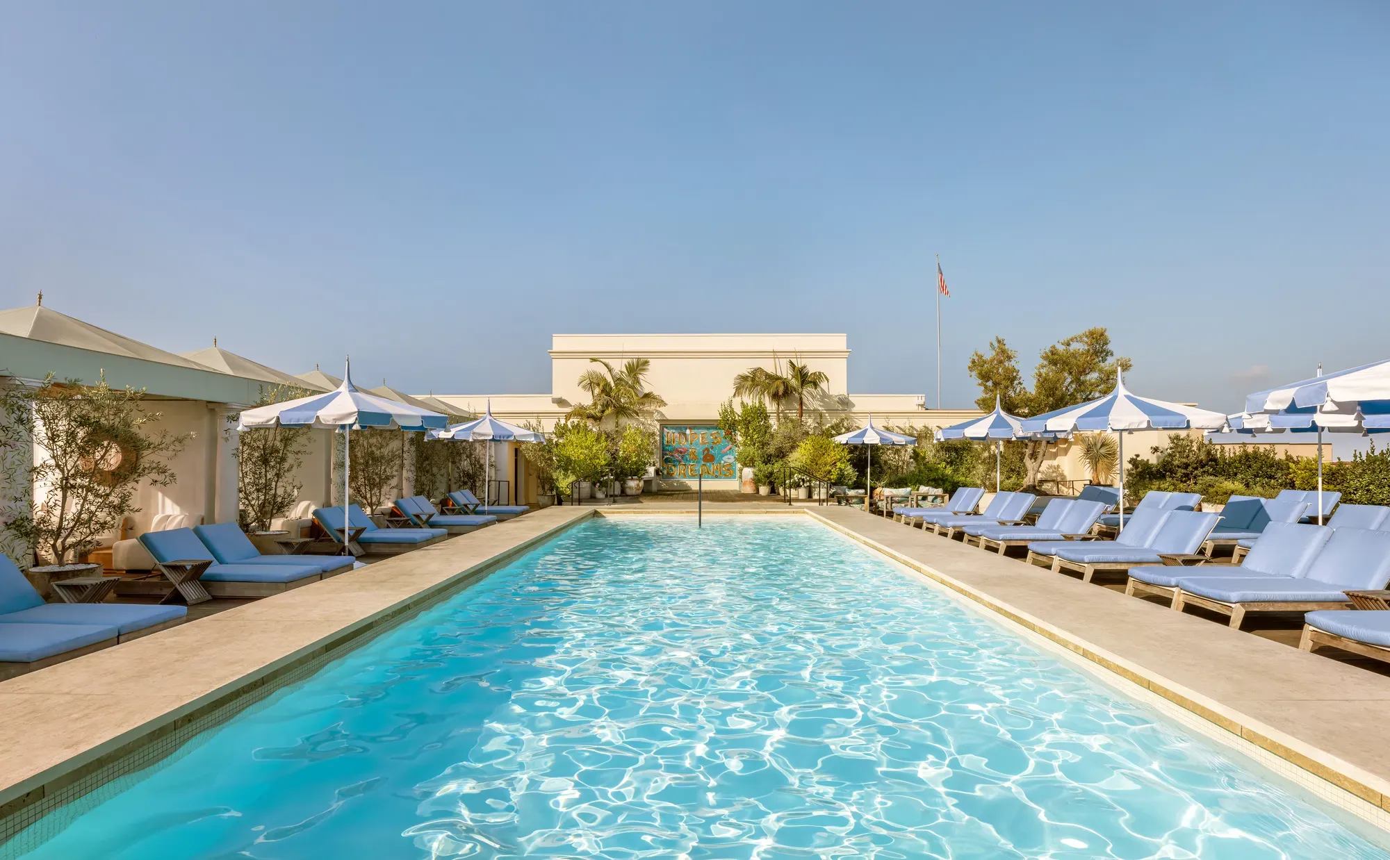 Lap-style rooftop pool at The Maybourne Beverly Hills lined with cabanas and blue-and-white umbrellas.