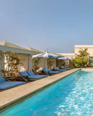 Lap-style rooftop pool at The Maybourne Beverly Hills lined with cabanas and blue-and-white umbrellas.