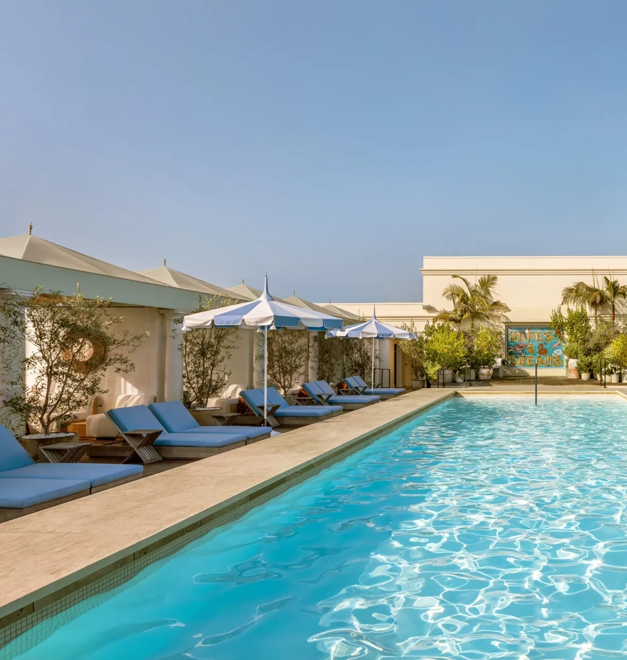 Lap-style rooftop pool at The Maybourne Beverly Hills lined with cabanas and blue-and-white umbrellas.
