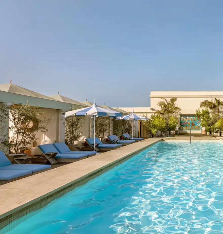 Lap-style rooftop pool at The Maybourne Beverly Hills lined with cabanas and blue-and-white umbrellas.