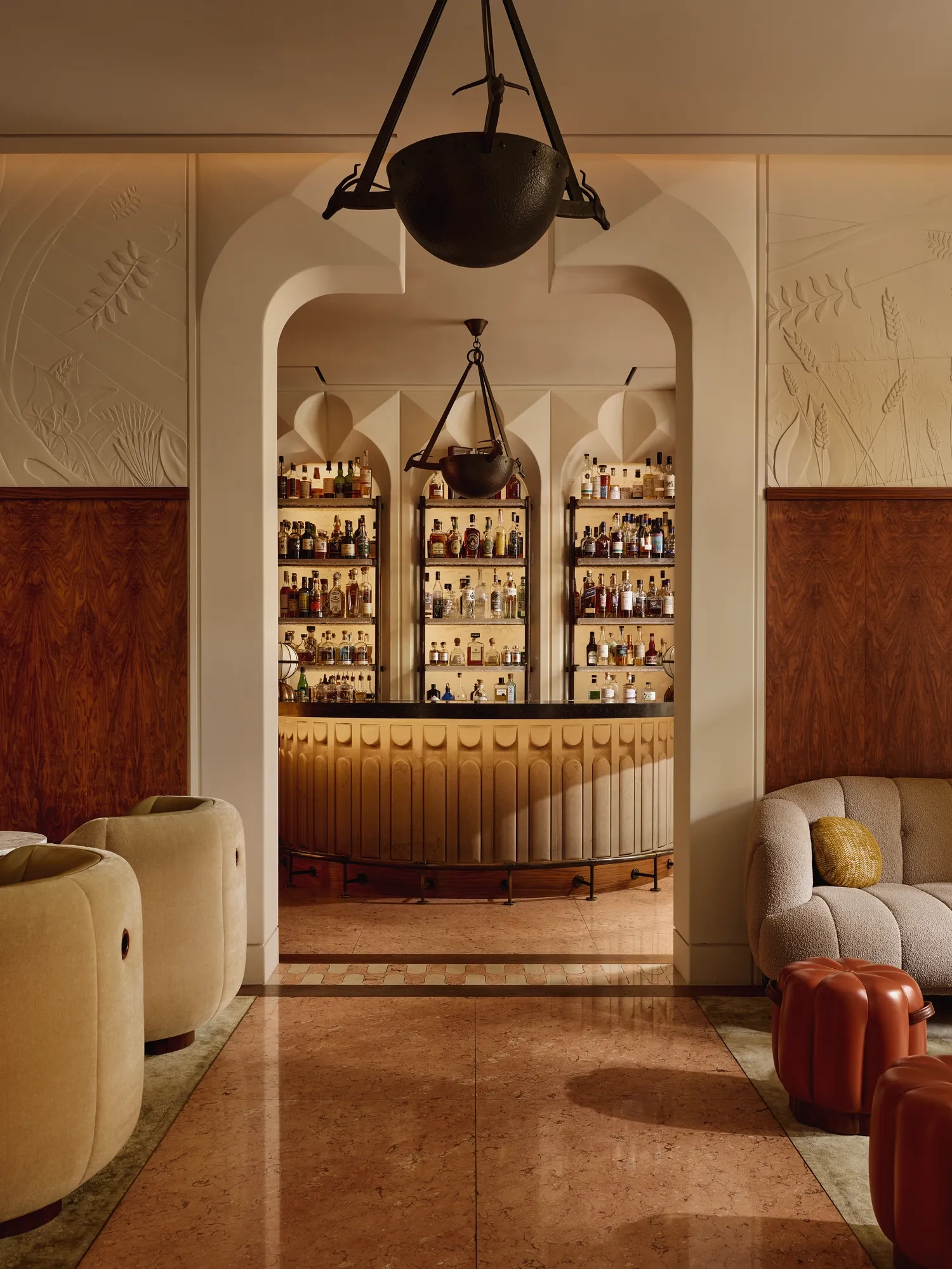 Stylish hotel bar with curved counter, art deco lighting, and display of premium spirits behind arched shelving.