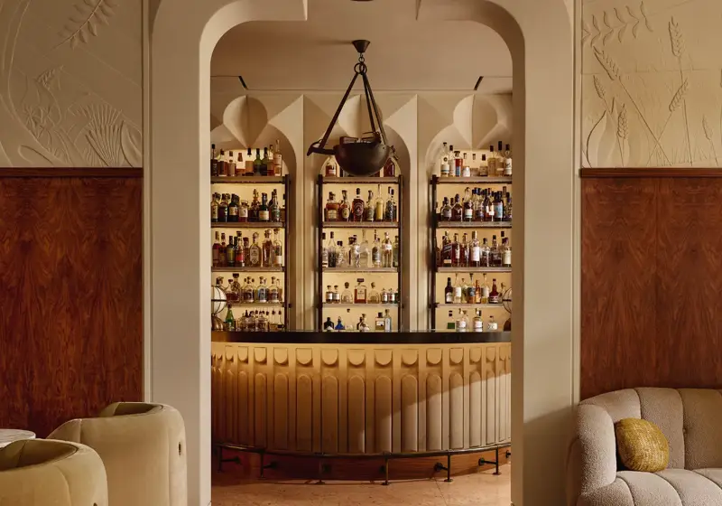 Stylish hotel bar with curved counter, art deco lighting, and display of premium spirits behind arched shelving.