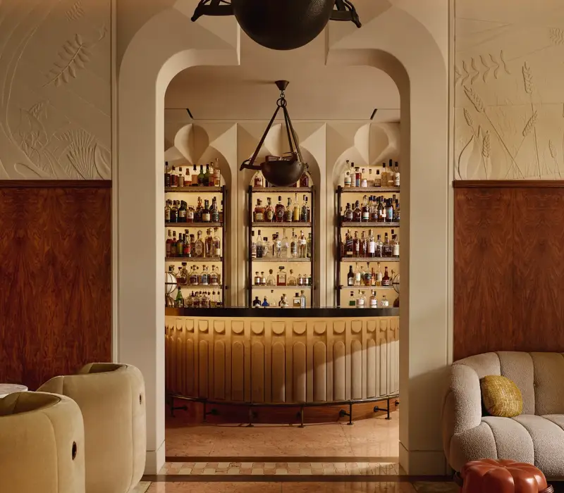 Stylish hotel bar with curved counter, art deco lighting, and display of premium spirits behind arched shelving.