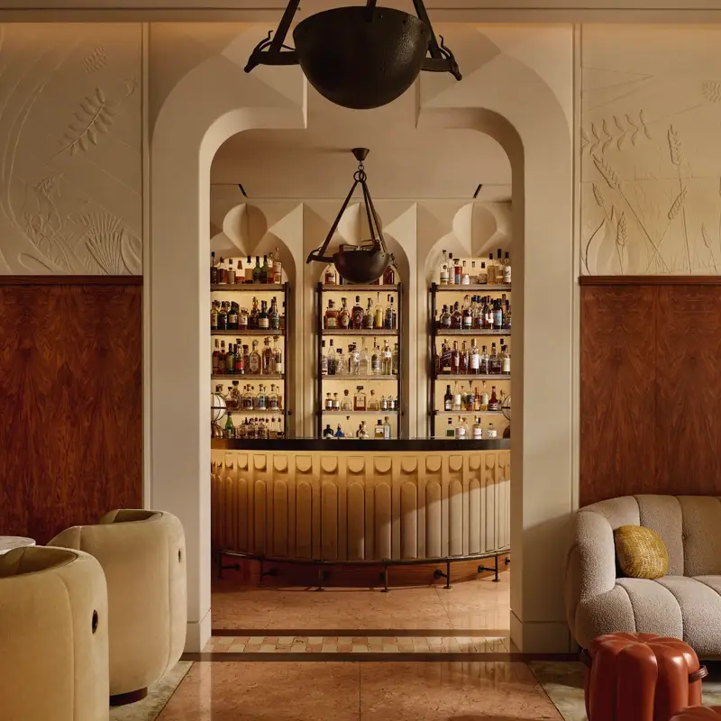 Stylish hotel bar with curved counter, art deco lighting, and display of premium spirits behind arched shelving.