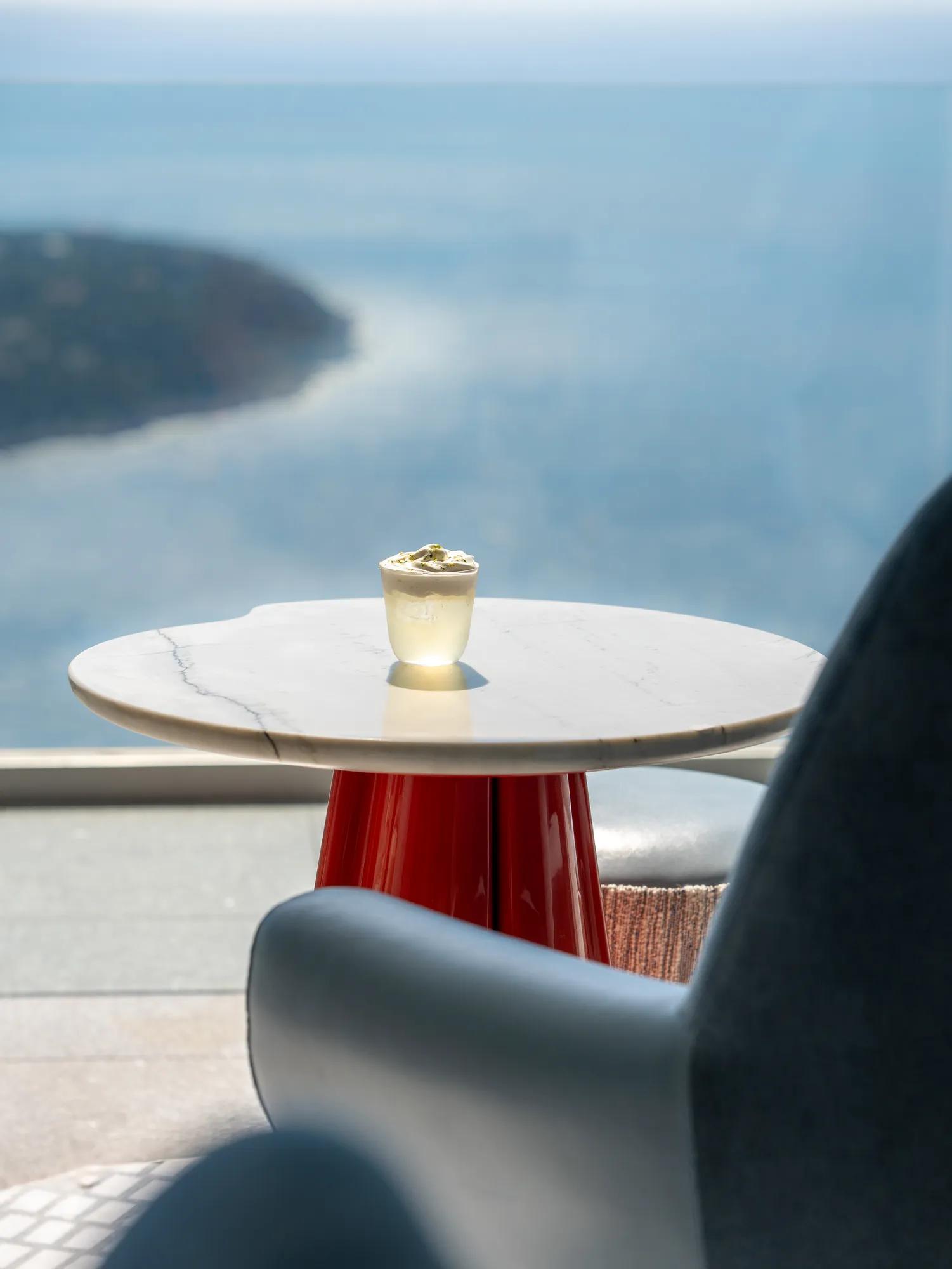 A drink on a marble table beside a lounge chair overlooking the sea and coastline.