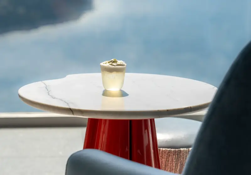 Une boisson sur une table en marbre face à un fauteuil avec vue sur la mer et la côte.
