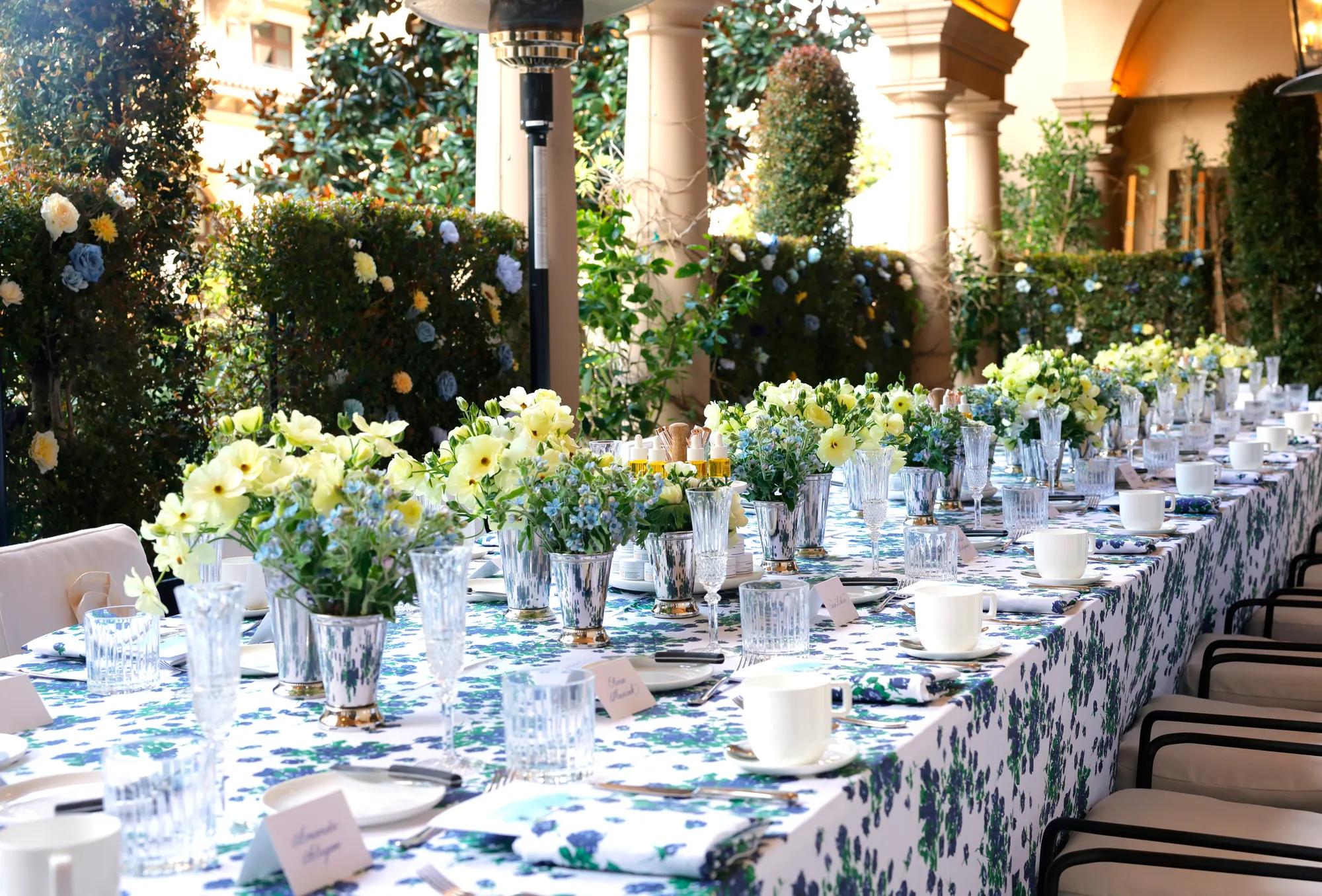 Kitchen Patio long table dressed in blue-floral linens with pastel centerpieces beneath an arched colonnade and garden hedges.