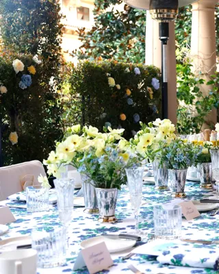 Kitchen Patio long table dressed in blue-floral linens with pastel centerpieces beneath an arched colonnade and garden hedges.