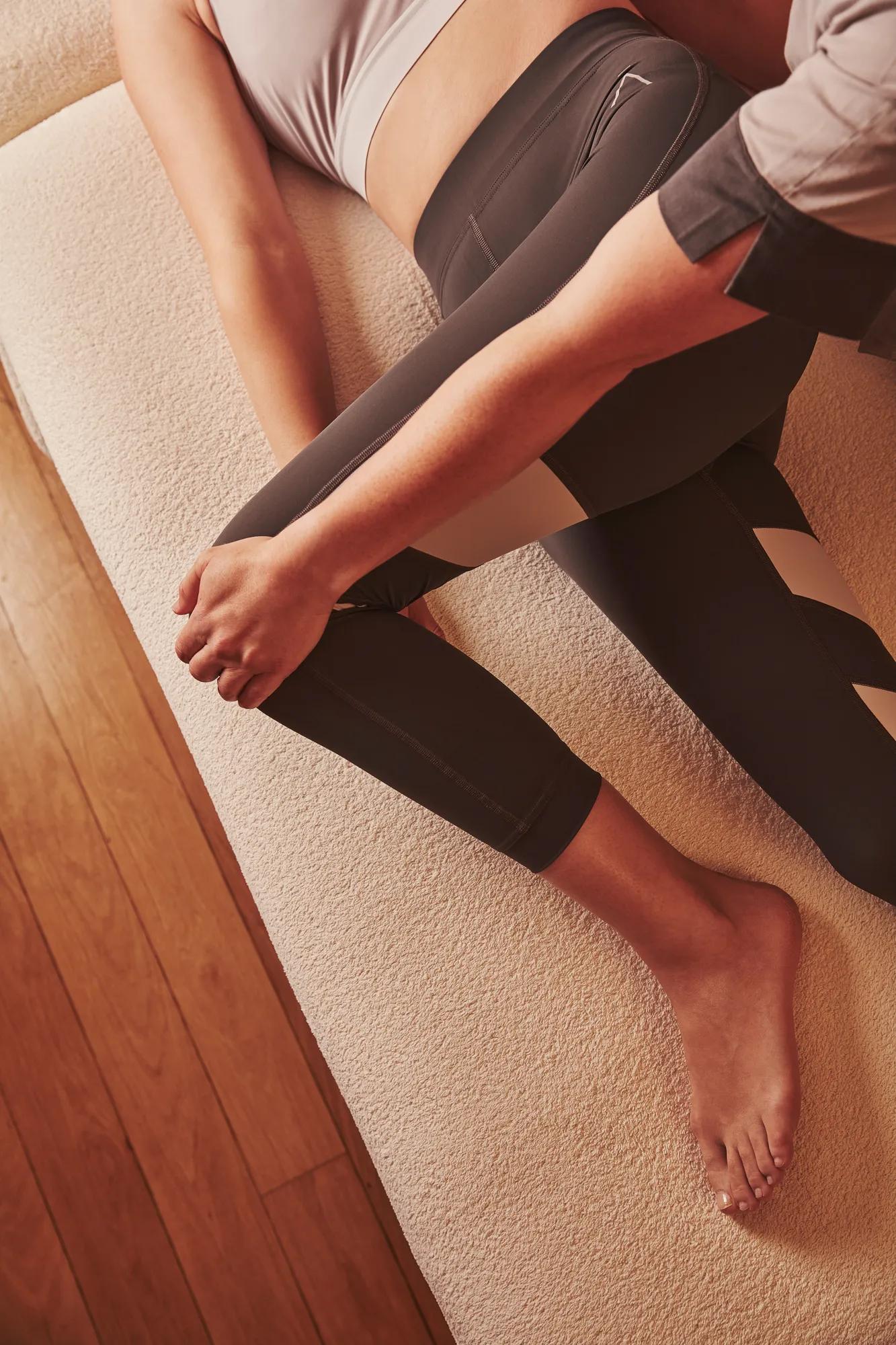 Therapist stretching a person's leg as they lie on a spa treatment bed in athletic wear.