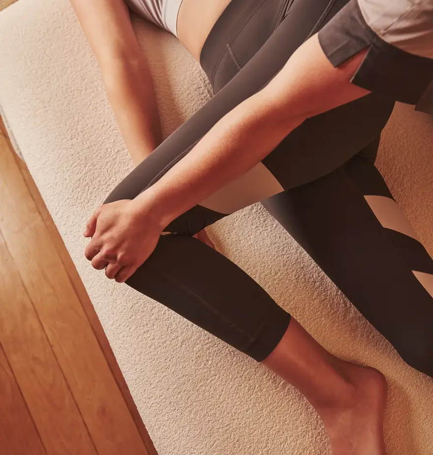 Therapist stretching a person's leg as they lie on a spa treatment bed in athletic wear.