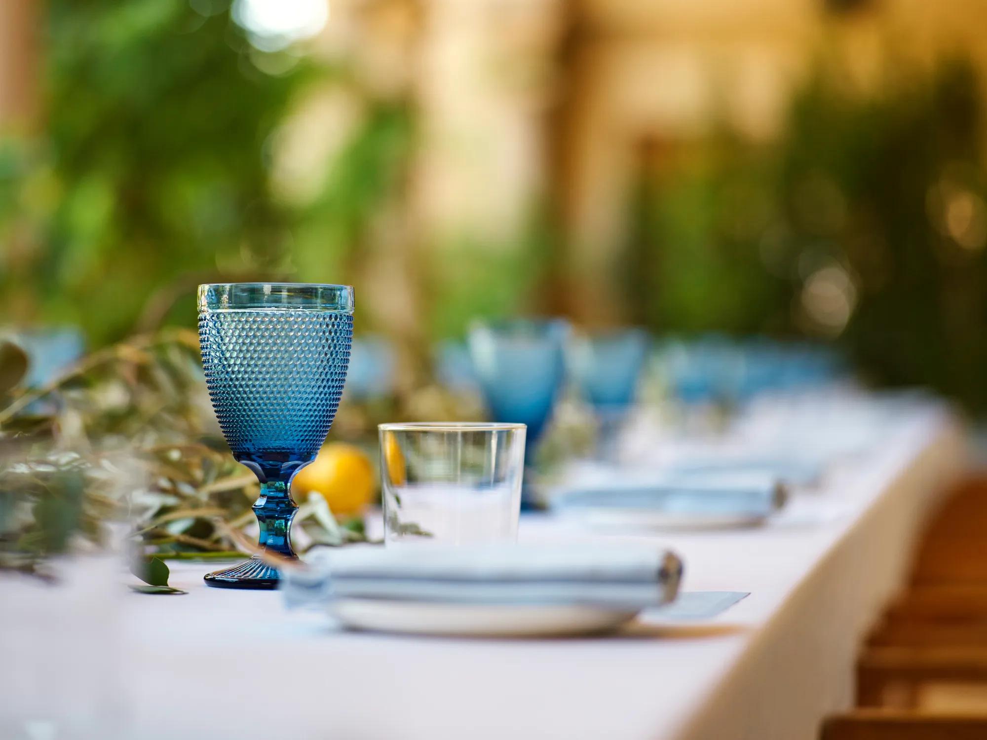 Close-up of a blue textured goblet and clear tumbler on the Kitchen Patio banquet table with a lemon-and-eucalyptus runner.