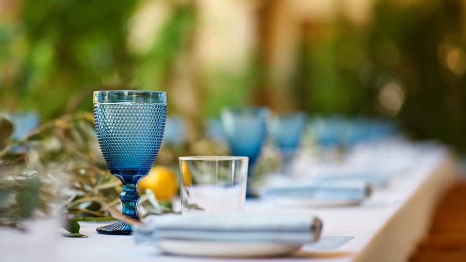 Close-up of a blue textured goblet and clear tumbler on the Kitchen Patio banquet table with a lemon-and-eucalyptus runner.