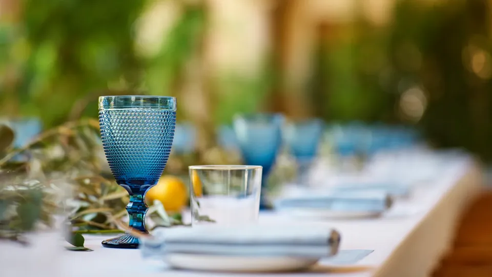 Close-up of a blue textured goblet and clear tumbler on the Kitchen Patio banquet table with a lemon-and-eucalyptus runner.