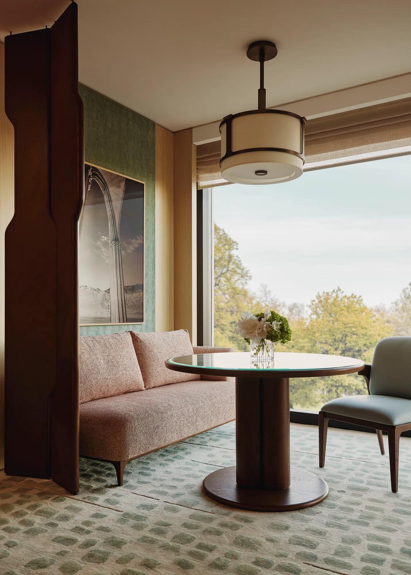 Dining nook with a round table, upholstered bench and chair, set beside a large window overlooking leafy treetops.
