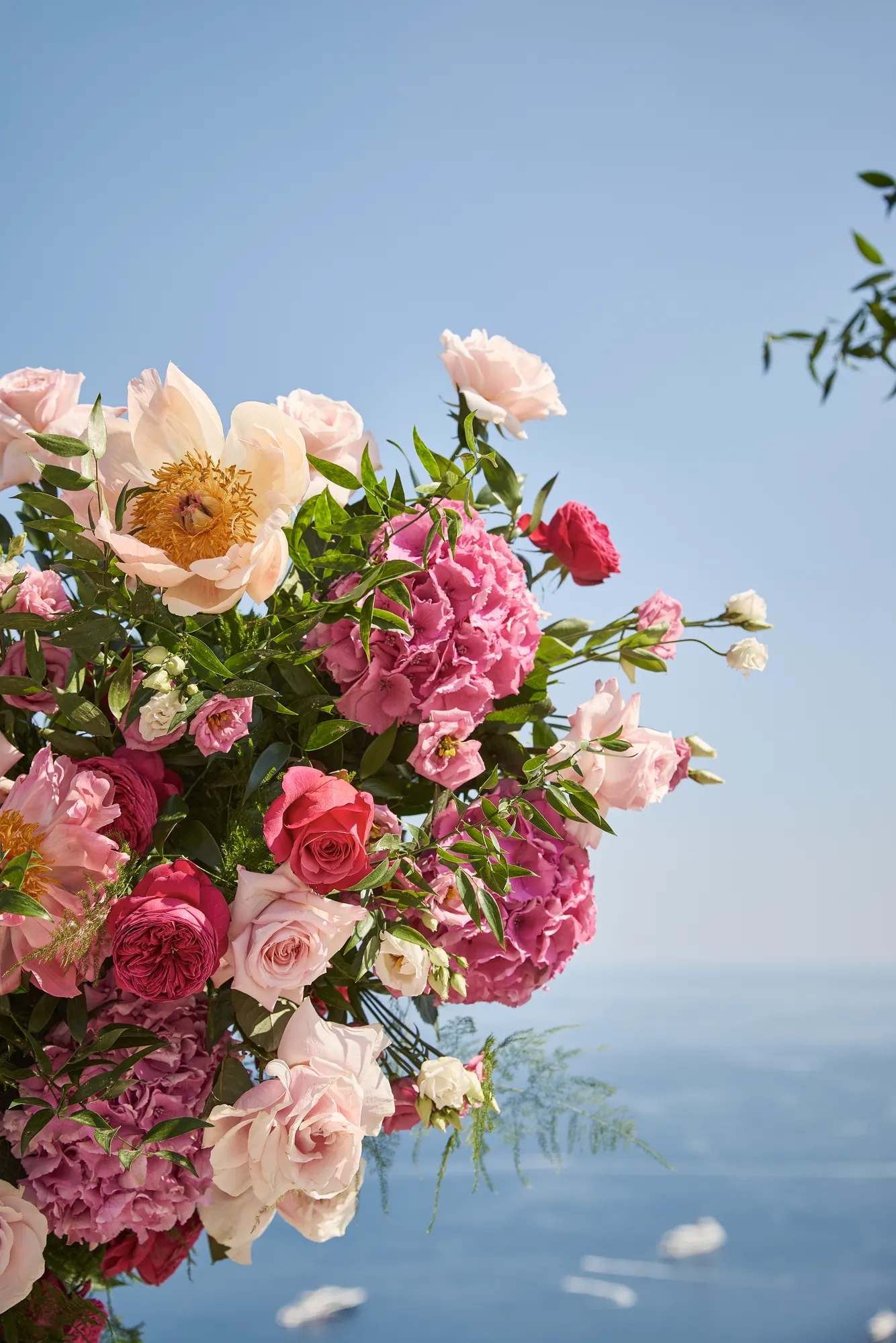 Close-up of pink and peach wedding flowers with ocean view and yachts in the distance under blue sky