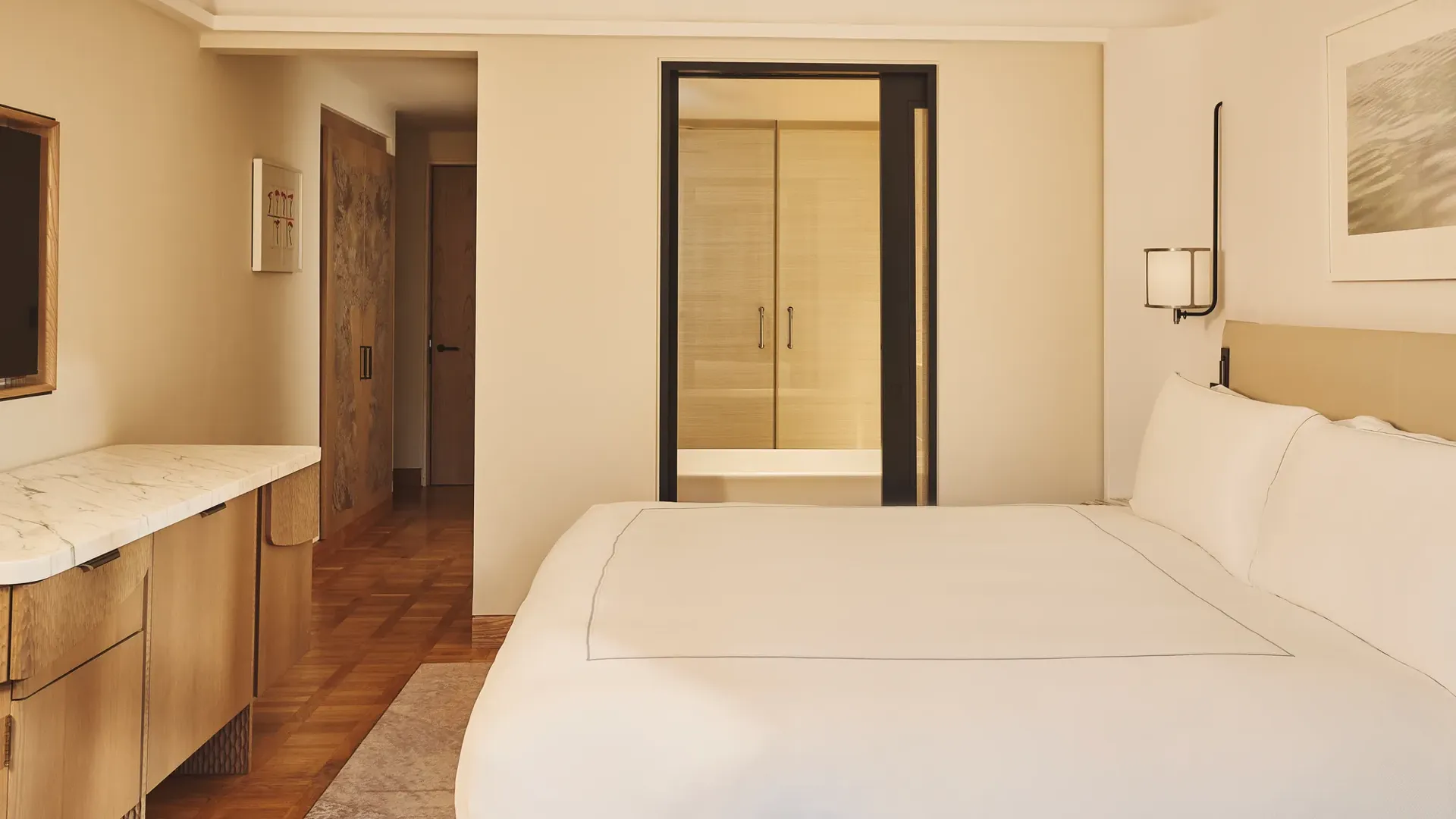 Minimal bedroom with king bed, marble desk, wood flooring, and view through to bathroom.
