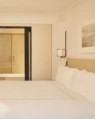 Minimal bedroom with king bed, marble desk, wood flooring, and view through to bathroom.
