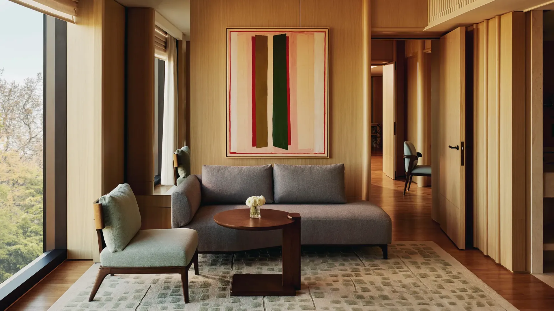 Compact seating area with grey sofa, abstract art, and a hallway view in The Emory Park Suite.