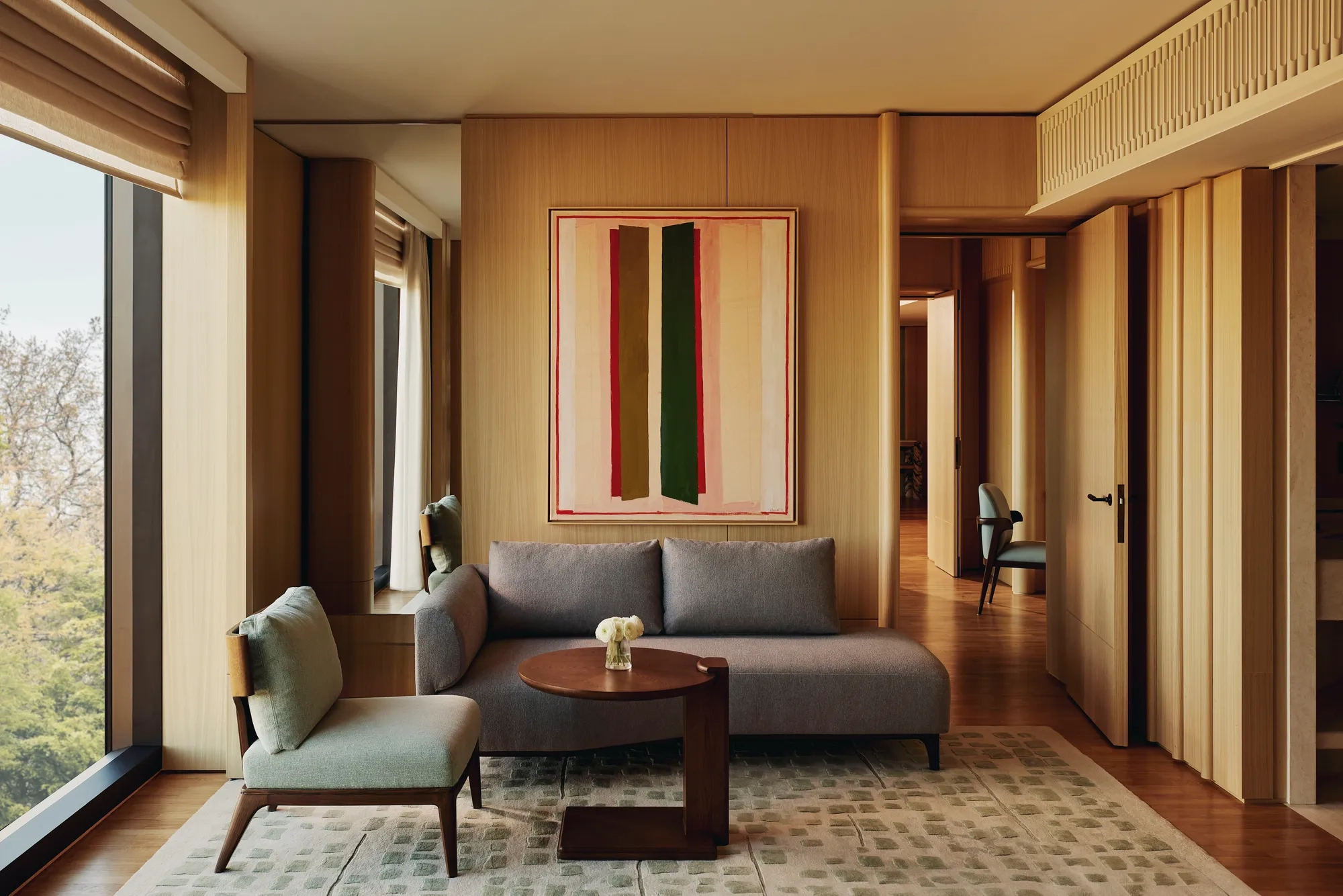 Compact seating area with grey sofa, abstract art, and a hallway view in The Emory Park Suite.