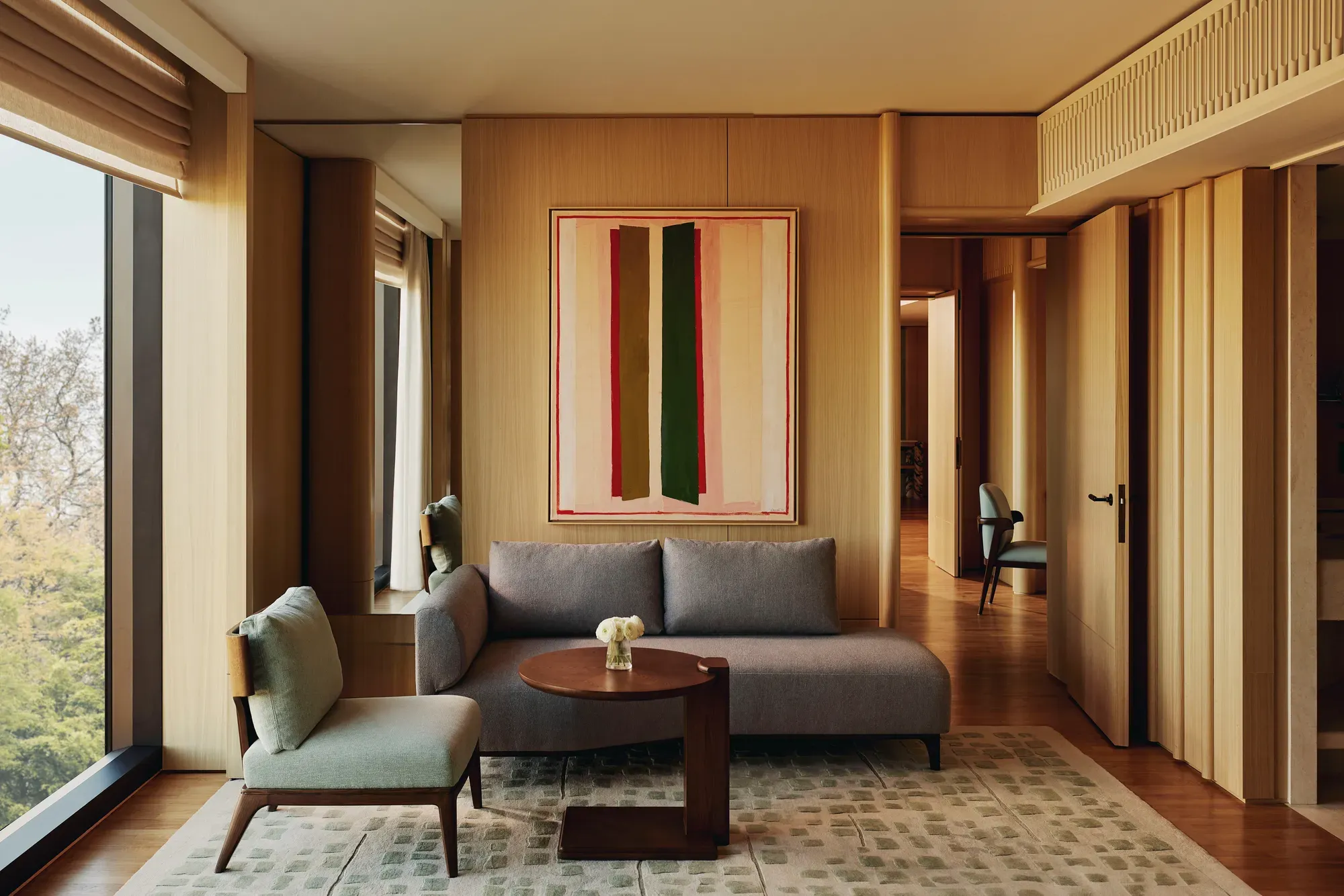 Compact seating area with grey sofa, abstract art, and a hallway view in The Emory Park Suite.
