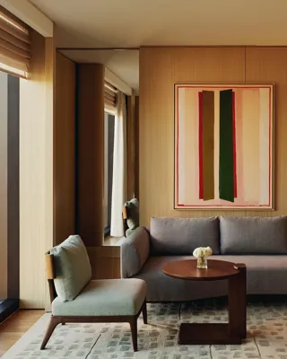 Compact seating area with grey sofa, abstract art, and a hallway view in The Emory Park Suite.