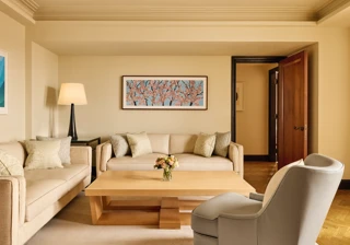 Bright living room with two cream sofas, a grey armchair, and a light wood coffee table topped with flowers, featuring a cherry blossom artwork on the wall above.