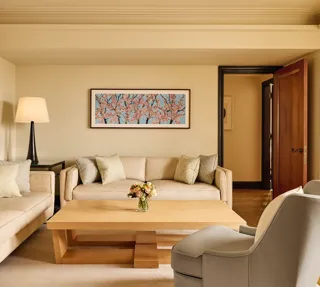Bright living room with two cream sofas, a grey armchair, and a light wood coffee table topped with flowers, featuring a cherry blossom artwork on the wall above.
