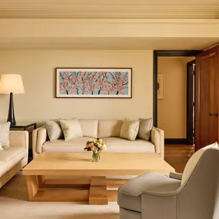Bright living room with two cream sofas, a grey armchair, and a light wood coffee table topped with flowers, featuring a cherry blossom artwork on the wall above.