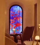 Lounge seating facing a tall arched window with vivid blue and red art glass.